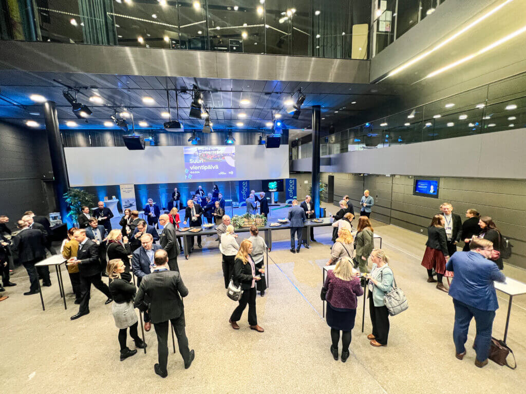 Ihmisiä keskustelemassa ja viettämässä yritystapahtumaa Musiikkitalon Alalämpiössä. Tilan digitaalisilla näytöillä näkyy päivän ohjelma ja tapahtumaan liittyviä videoita.