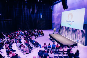 Yritystapahtuma Paavo-salissa. Ihmiset kuuntelevat puhujaa puolenkaaren muotoisessa katsomossa.