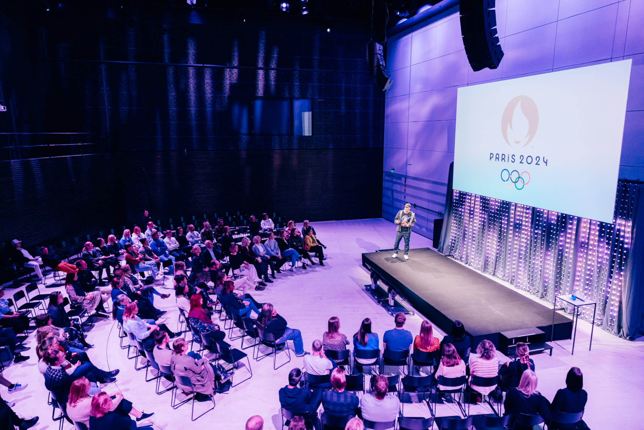 Yritystapahtuma Paavo-salissa. Ihmiset kuuntelevat puhujaa puolenkaaren muotoisessa katsomossa.