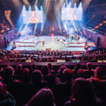 Suuri yritystapahtuma Musiikkitalon Konserttisalissa. Yleisö istuu salissa ja katsoo lavalla esiintyvää puhujaa.