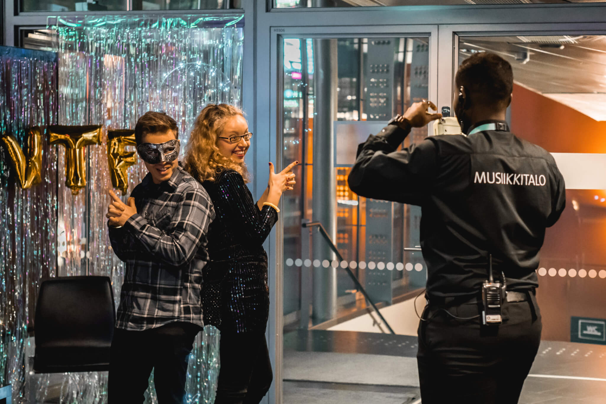 Pikkujoulujuhlijat poseeraavat kameralle Musiikkitalossa, ja järjestyksenvalvoja ottaa heistä valokuvan.